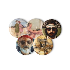 May include: A collection of five circular pin badges with watercolour-style illustrations. The designs include portraits of people and a dog on a motorcycle. The badges are in shades of brown, beige, and blue.