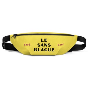 May include: A yellow fanny pack with black straps and a zipper. The text "LE SANS BLAGUE" is printed in black on the front of the pack. The words "CAFÉ" are printed in pink on either side of the text.