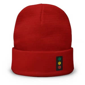 May include: A vibrant red beanie hat with a turned-up brim. The hat has a small, rectangular patch on the brim displaying a traffic light design: green, amber, and red lights.