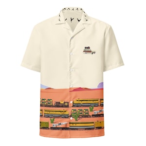 May include: A beige short-sleeved button-down shirt with a vintage car and train print. The car is brown and has luggage on the roof. The train is yellow and has multiple cars. The background is a desert landscape with cacti.