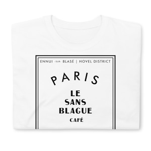 May include: White t-shirt with a black graphic design that says "Paris Le Sans Blague Cafe" with the text "Ennui -sur- Blasé | Hovel District" above it.