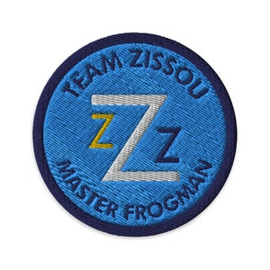Puede incluir: Parche bordado con fondo azul y borde azul marino. El parche presenta el texto "TEAM ZISSOU MASTER FROGMAN" en blanco y la letra "Z" en blanco, amarillo y azul marino.