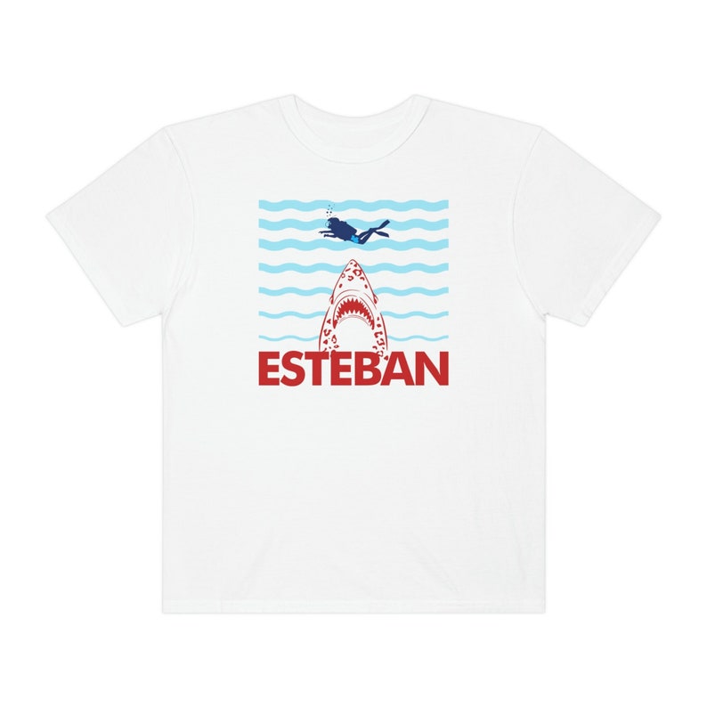 May include: White t-shirt with a red shark graphic and the word "ESTEBAN" in red letters. A blue silhouette of a person diving is above the shark.
