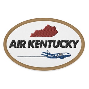 Può includere: Una toppa ovale bianca con un bordo marrone. La toppa presenta un contorno rosso ricamato dello stato del Kentucky, il testo "AIR KENTUCKY" in nero e un aereo blu e bianco che vola sopra una linea bianca.