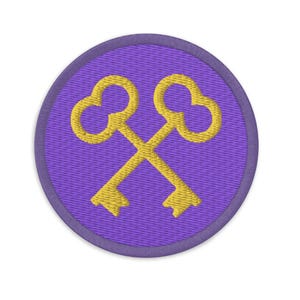May include: A purple round patch with a yellow embroidered design of two crossed keys.