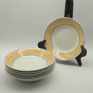 May include: A set of five white ceramic soup bowls with a yellow, blue, and green rim design. The bowls are stacked on top of each other.