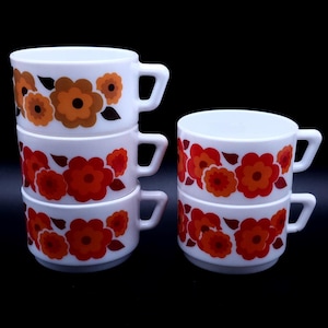 May include: Four white ceramic mugs with a floral pattern in shades of orange, red, and brown. The mugs are stacked on top of each other.
