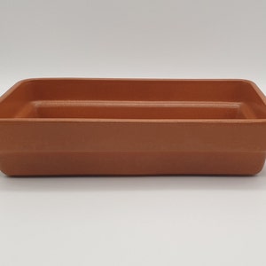 May include: A terracotta rectangular planter with a raised lip around the top edge. The planter has a smooth, unglazed finish.