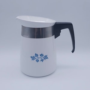 May include: White ceramic coffee pot with a blue floral design and a black handle. The pot has a silver band around the middle.