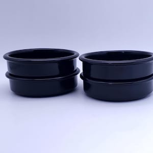 May include: Two stacks of two black ceramic ramekins, totaling four individual round dishes. Each ramekin features a smooth, glossy finish with a slightly flared rim at the top, designed for serving or baking individual portions in a kitchen setting.