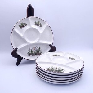 May include: A set of round, white ceramic divided plates with a speckled finish and a brown rim. Each plate features a central circular section surrounded by four smaller compartments, decorated with green fern and botanical illustrations.