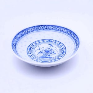 Könnte beinhalten: Eine kleine, weiße Keramikschale mit einem blauen und weißen Blumendesign. Die Schale hat einen gewellten Rand und einen erhöhten Rand.