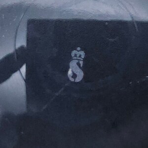 Peut inclure: Gros plan sur une surface noire avec une lettre 'S' stylis&eacute;e blanche surmont&eacute;e d'une couronne.