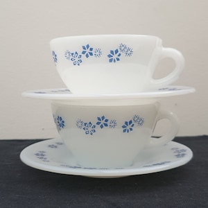 May include: A white ceramic teacup and saucer set with a blue snowflake pattern.