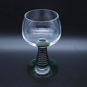 May include: A clear glass wine glass with a green base and a black, ribbed stem.