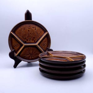 Op de afbeelding: Een set van vijf ronde bruine keramische verdeelborden met een glanzende afwerking. Elk bord heeft drie afzonderlijke secties gescheiden door verhoogde randen, met geometrische en cirkelvormige patronen in reliëf op het oppervlak.