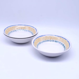 May include: Two white ceramic bowls with a blue and yellow patterned rim. The bowls are stacked on top of each other.