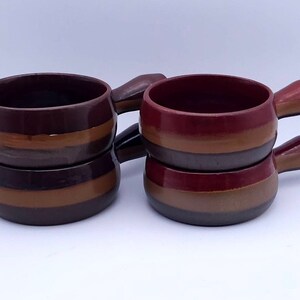 Op de afbeelding: Set van vier bruin en rood gestreepte keramische ramekins met handvatten. Elk ramekin heeft drie strepen in bruin, beige en rood.