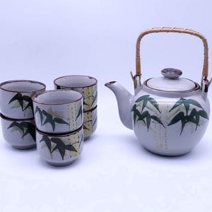 May include: A white ceramic teapot with a bamboo design and a brown wicker handle, along with four matching teacups.