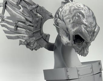 May include: A gray, 3D-printed sculpture of a creature with a skull-like head, detailed wings, and a box-like base. The sculpture has a textured surface and is made of a solid, gray material. The wings are intricate and detailed.