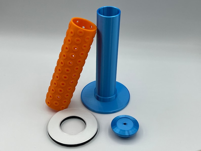 May include: A set of 3D printed parts for a 3D printer. The set includes a blue tube with a base, a white ring with a black inner ring, and a blue cap. The tube has a textured surface with small holes.