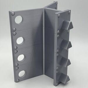 May include: A gray metal stand with four triangular spikes on one side and five round holes on the other side.