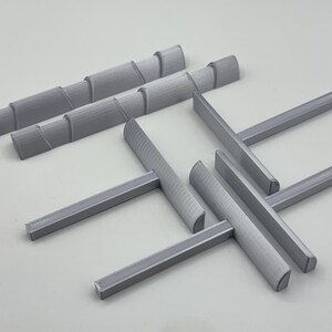 May include: A collection of gray 3D-printed objects, including several rectangular bars and cylindrical pieces with a spiral design. The objects are arranged on a light gray surface.