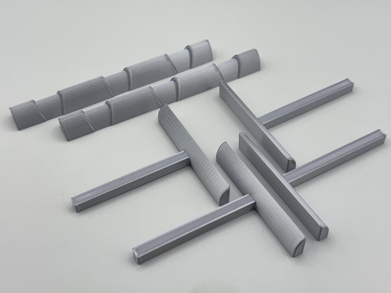 May include: A collection of gray 3D-printed objects, including several rectangular bars and cylindrical pieces with a spiral design. The objects are arranged on a light gray surface.