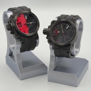 May include: Two black wristwatches with a red and black dial, displayed on gray stands. The watches have a black strap and a large, round face. One watch has a red and black dial, while the other has a black dial with red accents. The number 9 is visible on both.