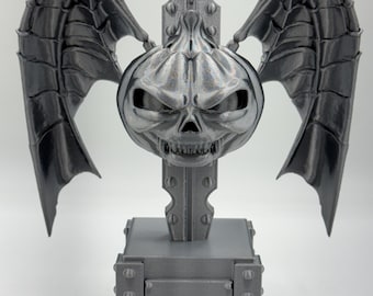 May include: A silver-colored, 3D-printed sculpture featuring a pumpkin-shaped skull with bat-like wings. The sculpture is mounted on a rectangular base with rivet details, and a vertical support structure.