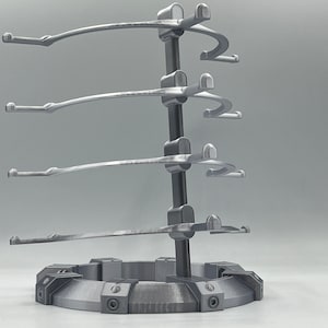 May include: A silver metal stand with four curved arms for displaying items. The stand has a circular base with a textured surface.