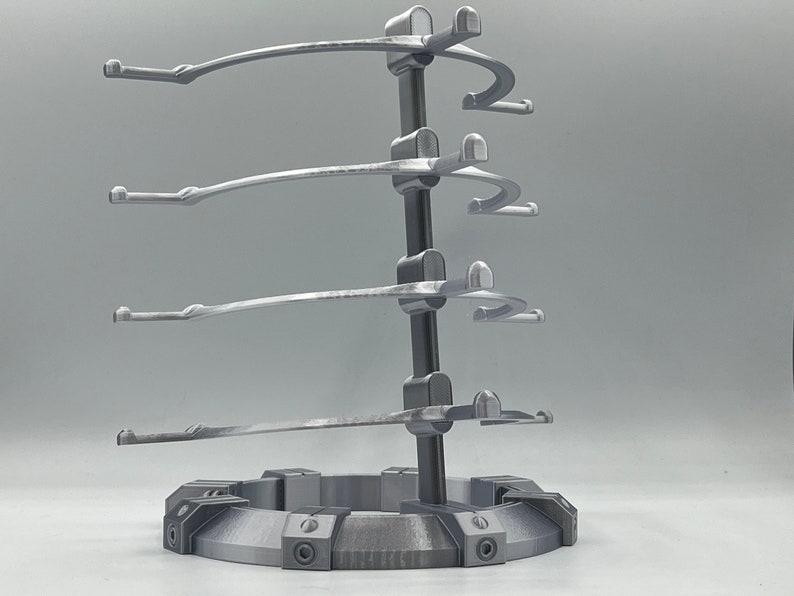 May include: A silver metal stand with four curved arms for displaying items. The stand has a circular base with a textured surface.