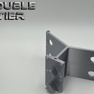 May include: A gray 3D printed double tier stand with a triangular base and three holes on each side. The stand has a textured surface and is designed to hold objects.