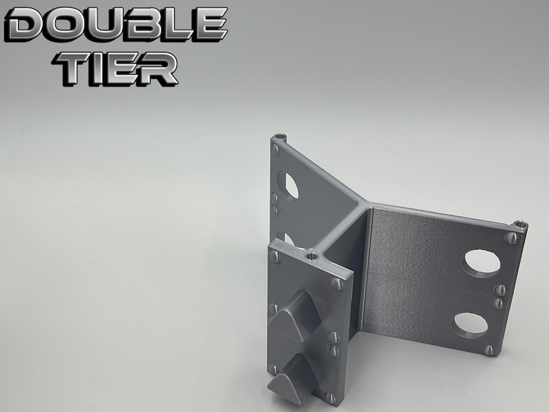 May include: A gray 3D printed double tier stand with a triangular base and three holes on each side. The stand has a textured surface and is designed to hold objects.