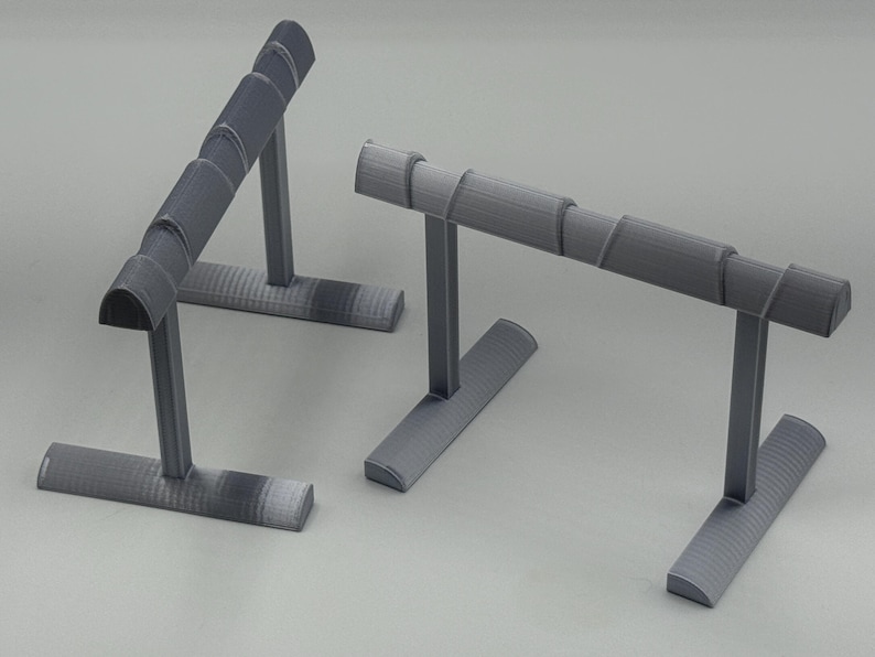 May include: Two gray jewelry display stands. Each stand has a rectangular base, a vertical support, and a curved top designed to hold jewelry. The stands are made of a textured material and are set against a neutral background.