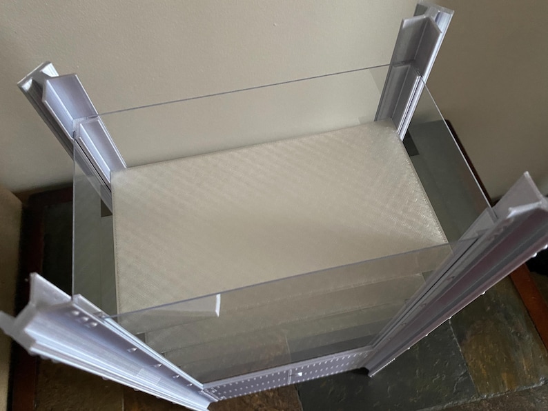 K&ouml;nnte beinhalten: Eine transparente, rechteckige Vitrine mit wei&szlig;em Innenraum und einer schr&auml;gen, transparenten Oberseite. Der Rahmen ist wei&szlig; und hat eine Reihe kleiner L&ouml;cher an den Kanten. Die Vitrine dient zur Pr&auml;sentation von Artikeln.