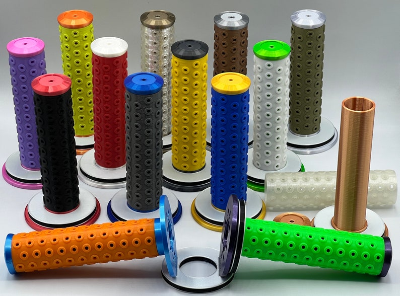 May include: A collection of 12 colorful motorcycle grips with a textured surface and a variety of colors, including purple, black, red, gray, yellow, blue, white, green, and brown. The grips are displayed on a white surface.