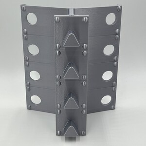 May include: A gray metal object with a series of triangular spikes on the front. The object has a series of holes on each side.