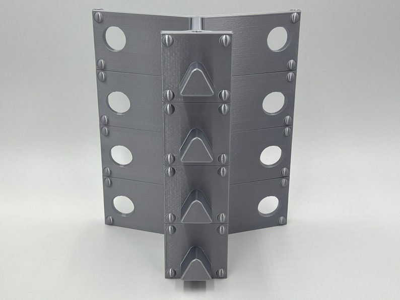 May include: A gray metal object with a series of triangular spikes on the front. The object has a series of holes on each side.