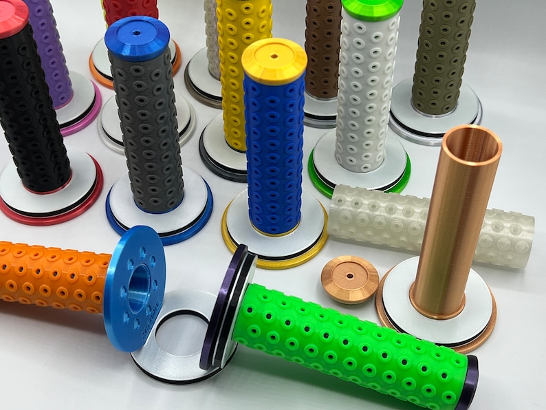 May include: Assortment of colorful motorcycle grips with different patterns and textures. The grips are displayed on white bases with black trim.