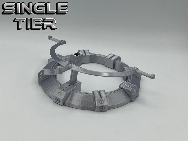 May include: A single-tier, silver-colored, 3D printed display stand with a circular base and a curved arm. The text "SINGLE TIER" is printed in black letters on a white background.