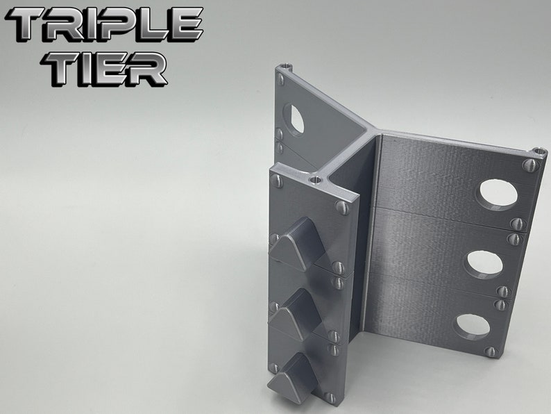 May include: A gray, three-tiered, 3D printed stand with a triangular shape. The stand has three slots on each side for holding items.