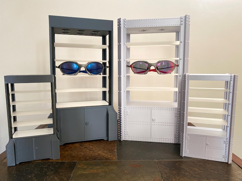 K&ouml;nnte beinhalten: Ausstellungsregale in verschiedenen Gr&ouml;&szlig;en, grau und wei&szlig; lackiert, mit mehreren Regalb&ouml;den und Schrankt&uuml;ren. Zwei Sonnenbrillen mit blauen und roten Gl&auml;sern werden pr&auml;sentiert. Die Regale sind f&uuml;r die Einzelhandelspr&auml;sentation konzipiert.