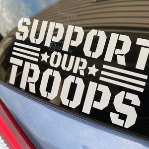 May include: White vinyl sticker on a car window that reads "Support Our Troops" with three white stripes and two stars.
