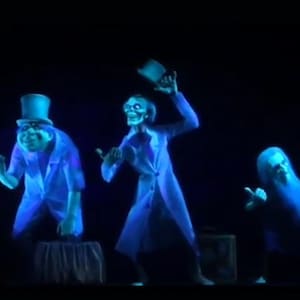 May include: Three ghostly figures in a dark setting. The figures are illuminated with a blue glow, resembling apparitions. One figure wears a top hat, another holds a hat aloft, and the third points. The scene evokes a spooky, spectral theme.