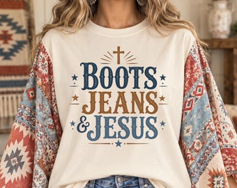 Könnte beinhalten: Ein cremefarbenes T-Shirt mit einem Grafikdruck, der "BOOTS JEANS & JESUS" in blauem und braunem Text mit einem Kreuzsymbol zeigt. Die Ärmel haben ein mehrfarbiges Muster in Rot-, Blau- und Weißtönen mit geometrischen Formen.