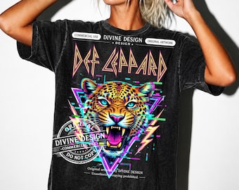 Può includere: Una t-shirt nera lavaggio acido con la grafica di un leopardo dagli occhi blu brillante e la bocca aperta. Il design include il testo "DEF LEPPARD" in un carattere stilizzato, il marchio "DIVINE DESIGN" e forme geometriche neon rosa e blu.