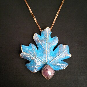 May include: A copper chain necklace with a blue and silver leaf pendant and a purple gemstone. The pendant is shaped like a maple leaf.