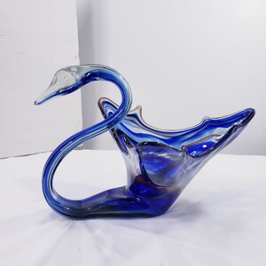 Puede incluir: Una escultura decorativa de cisne de cristal en tonos azules, con un pico transparente y un cuello curvado. El cisne tiene un cuerpo en forma de cuenco con un aspecto texturizado y en capas. Una pieza única de decoración del hogar.