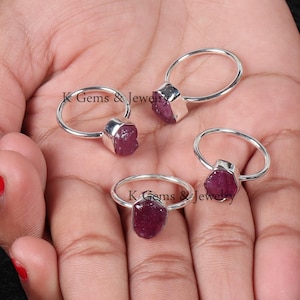 May include: Four silver rings with raw ruby gemstones. Each ring features a different shaped ruby, all with a deep pink hue.